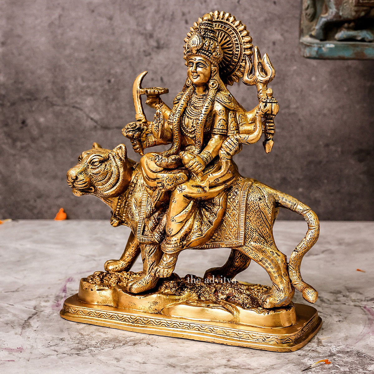 Left side view of brass Durga Mata Murti riding lion on base, displaying profile of goddess’s face, arms with weapons, and lion’s powerful stance.