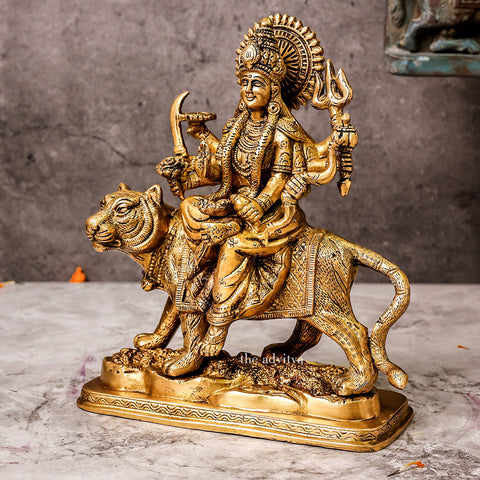 Left side view of brass Durga Mata Murti riding lion on base, displaying profile of goddess’s face, arms with weapons, and lion’s powerful stance.