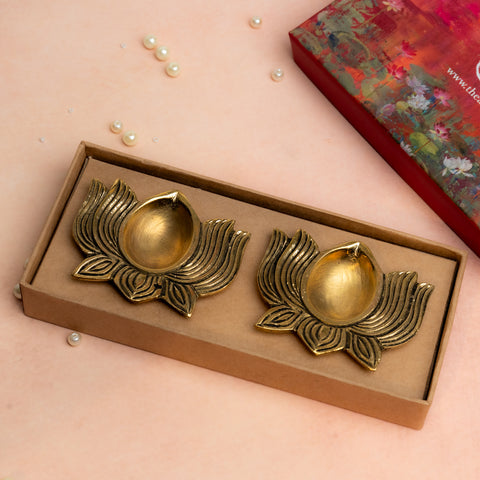 Brass lotus shaped diya set of 2 in golden finish placed in box on soft pastel background.