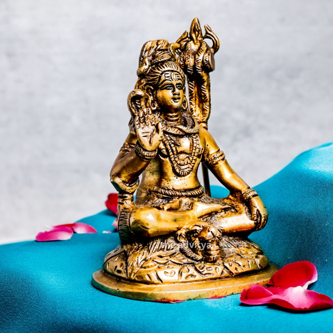Side angle of a small brass Shiva statue highlighting the trident and ornamental details.