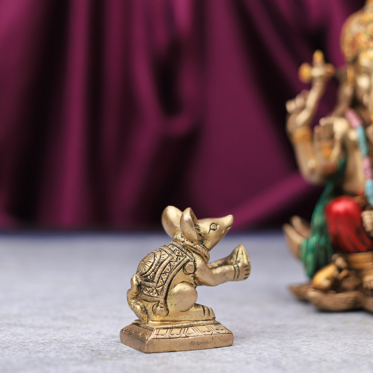 A brass figurine of Lord Ganesha in a mouse form, with intricate detailing, placed next to a larger statue of Lord Ganesha in a human form.
