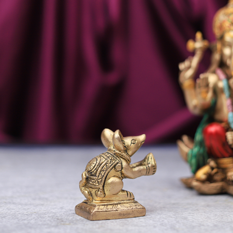 A brass figurine of Lord Ganesha in a mouse form, with intricate detailing, placed next to a larger statue of Lord Ganesha in a human form.