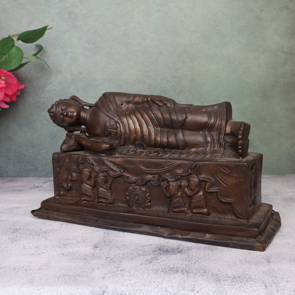 Handcrafted brass sleeping Buddha statue highlighting intricate robe and base carvings