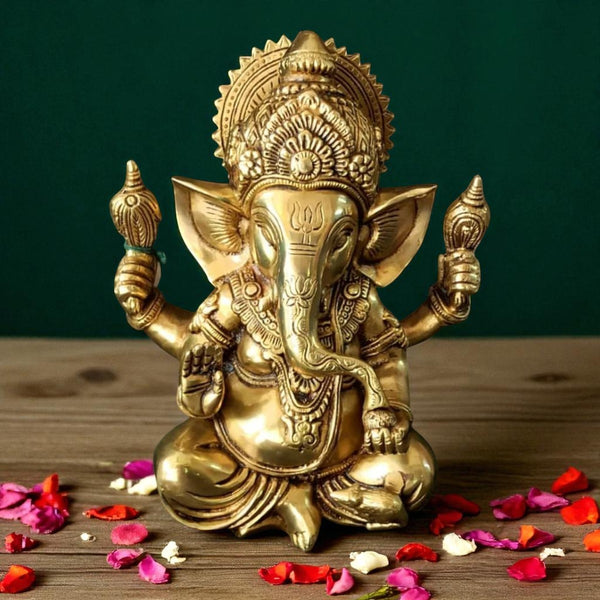 Brass Lord Ganesha idol placed on a wooden surface, decorated with scattered rose and marigold petals, against a dark green background