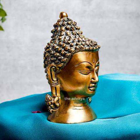 Right-angle view of a small Buddha head statue with a smooth brass finish.